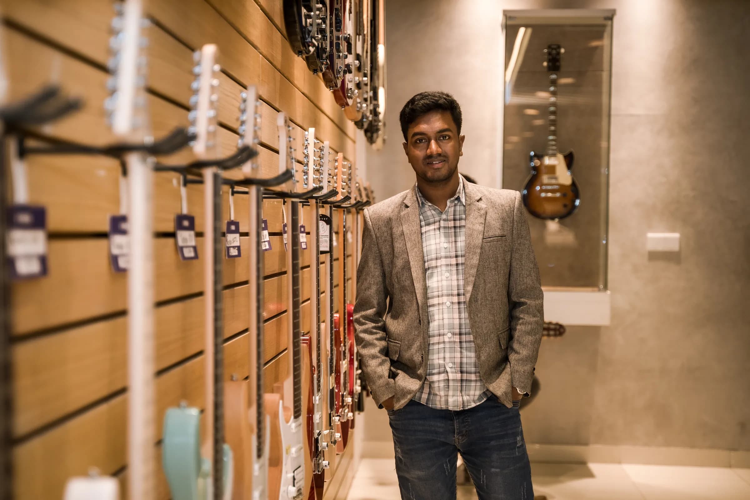 Razu Rahman standing beside a wall of guitars in a music showroom