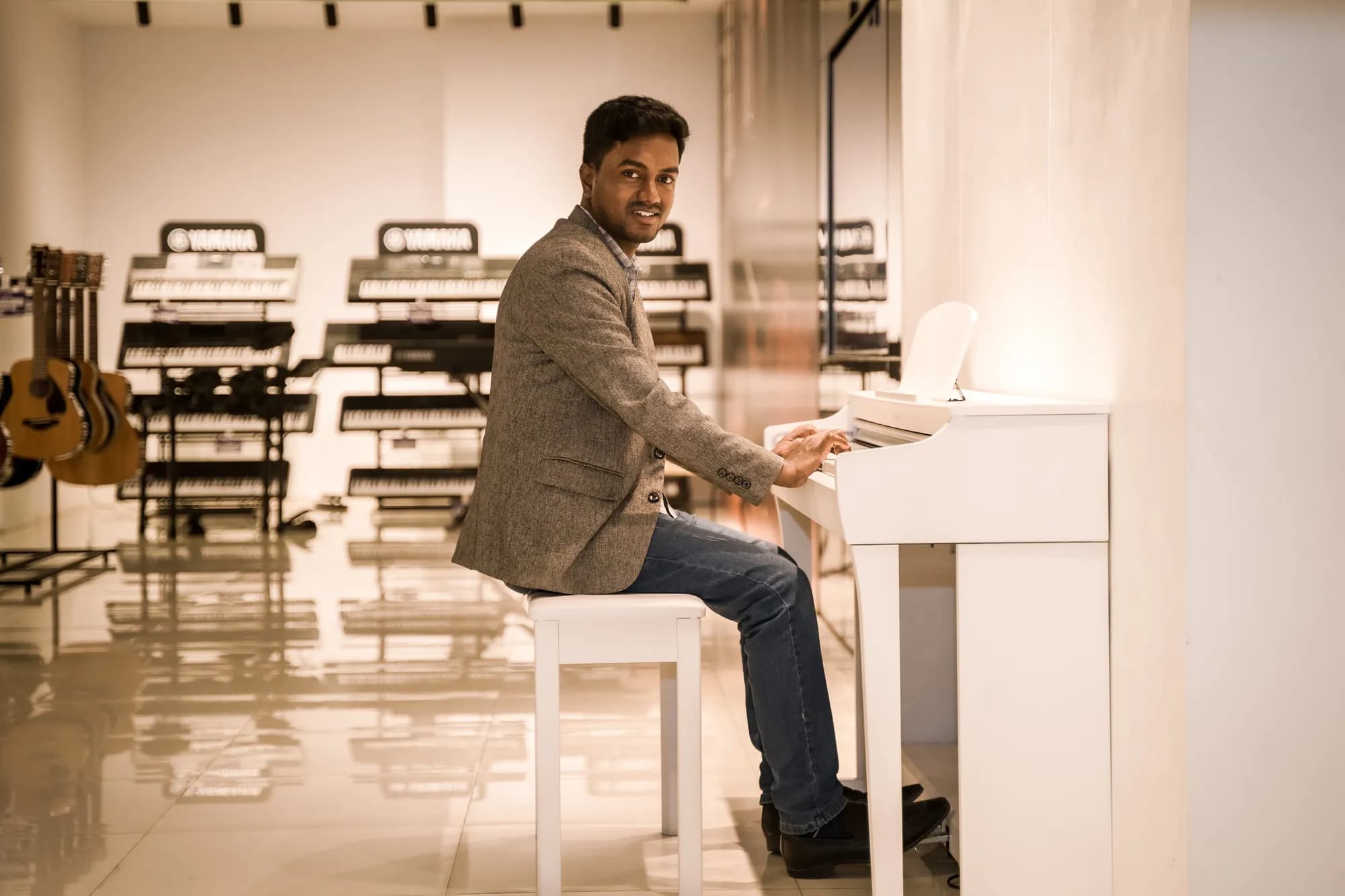 Razu Rahman seated at a white piano in a music showroom